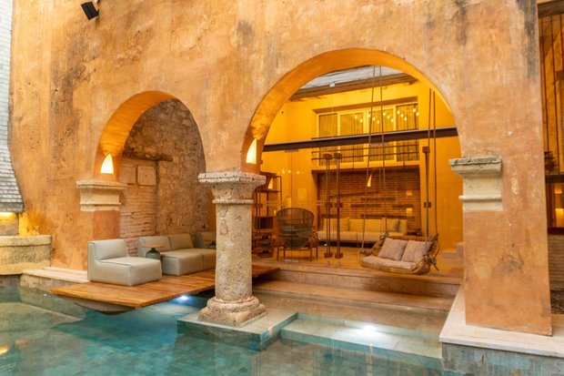 The courtyard at night: stone arches lit warm above a shallow pool, with a rope swing seat hanging over the water.