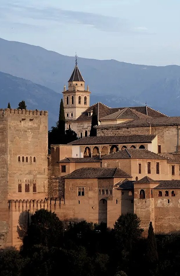 The Alhambra's towers and walls glowing at sunset, with the Sierra Nevada behind in blue haze.