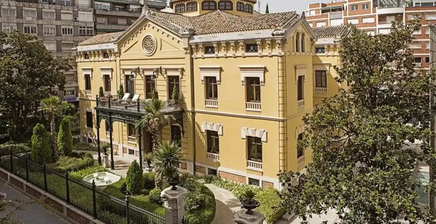 The palace from outside: a yellow 19th-century mansion with a tiled roof and lantern tower, an iron balcony and a formal garden behind railings.