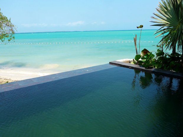 The dark edge of a plunge pool, and beyond it turquoise shallows running out to the horizon.