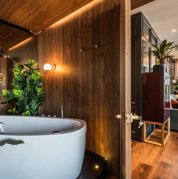 A suite: freestanding oval bathtub against walnut panelling, warm concealed lighting, opening through to the room.
