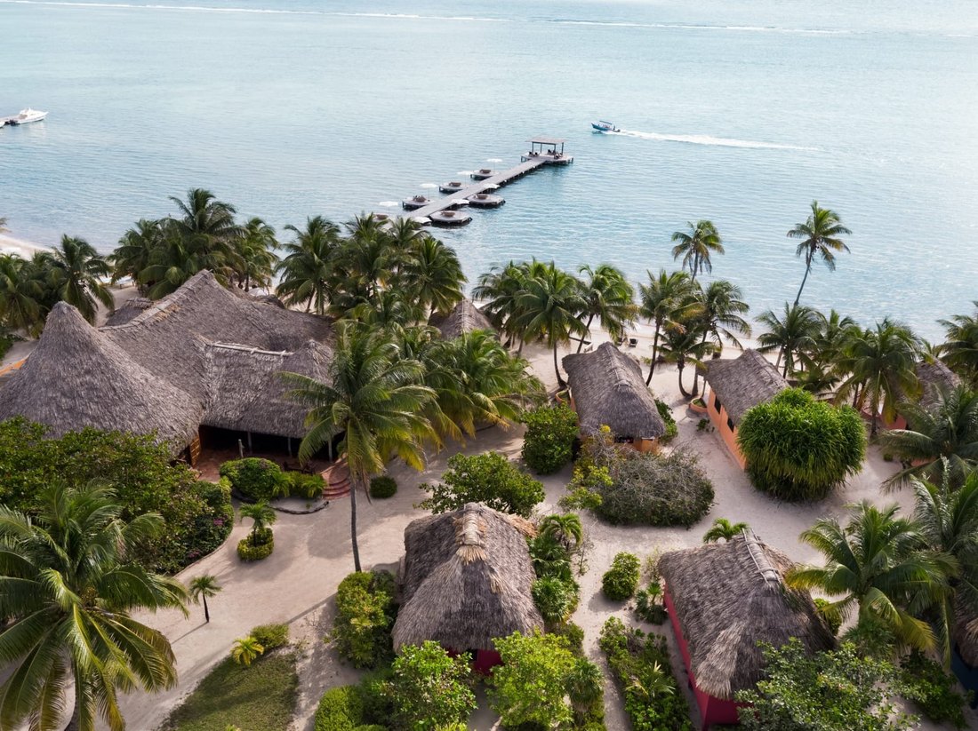 Matachica from the air: thatched casitas painted in bright colours among palms on white sand, and a long pier with daybeds running out over pale turquoise water.