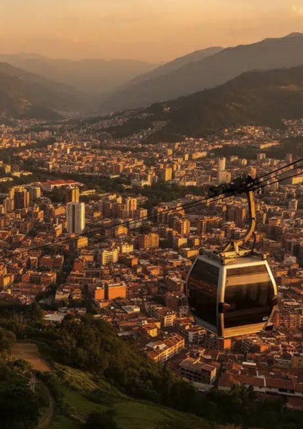 A Metrocable gondola hanging above the city at sunset, the whole valley of low orange rooftops running back to the mountains.