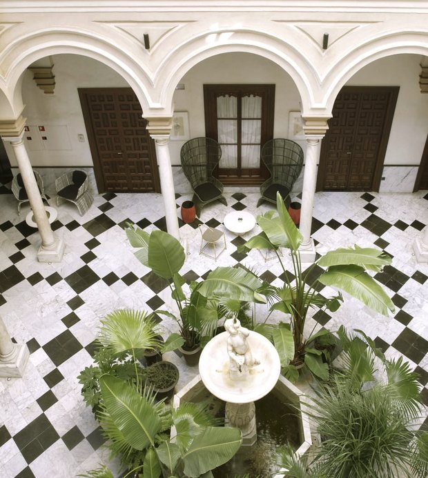 The courtyard from above: white arches, a black-and-white marble floor and a stone fountain among palms.