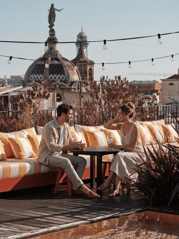 The roof terrace: striped orange sofas, string lights and a small pool, with Gothic Quarter domes behind.